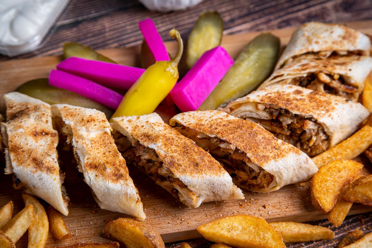 A sliced shawarma wrap with pickles and fries